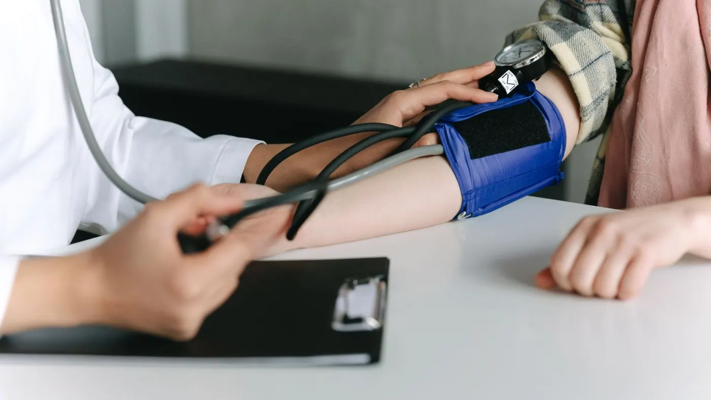Brazalete azul de un tensiómetro de aguja puesto en el brazo de un paciente durante la toma de la presión arterial en el consultorio