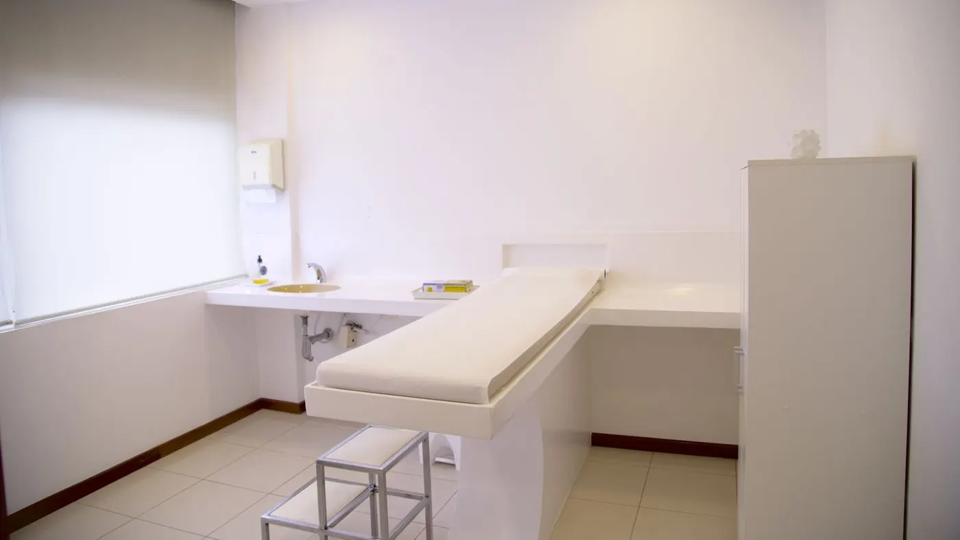 Consultorio médico vacío con camilla de examen, lavamanos y luz blanca, el lugar donde se toma la presión arterial en un examen médico