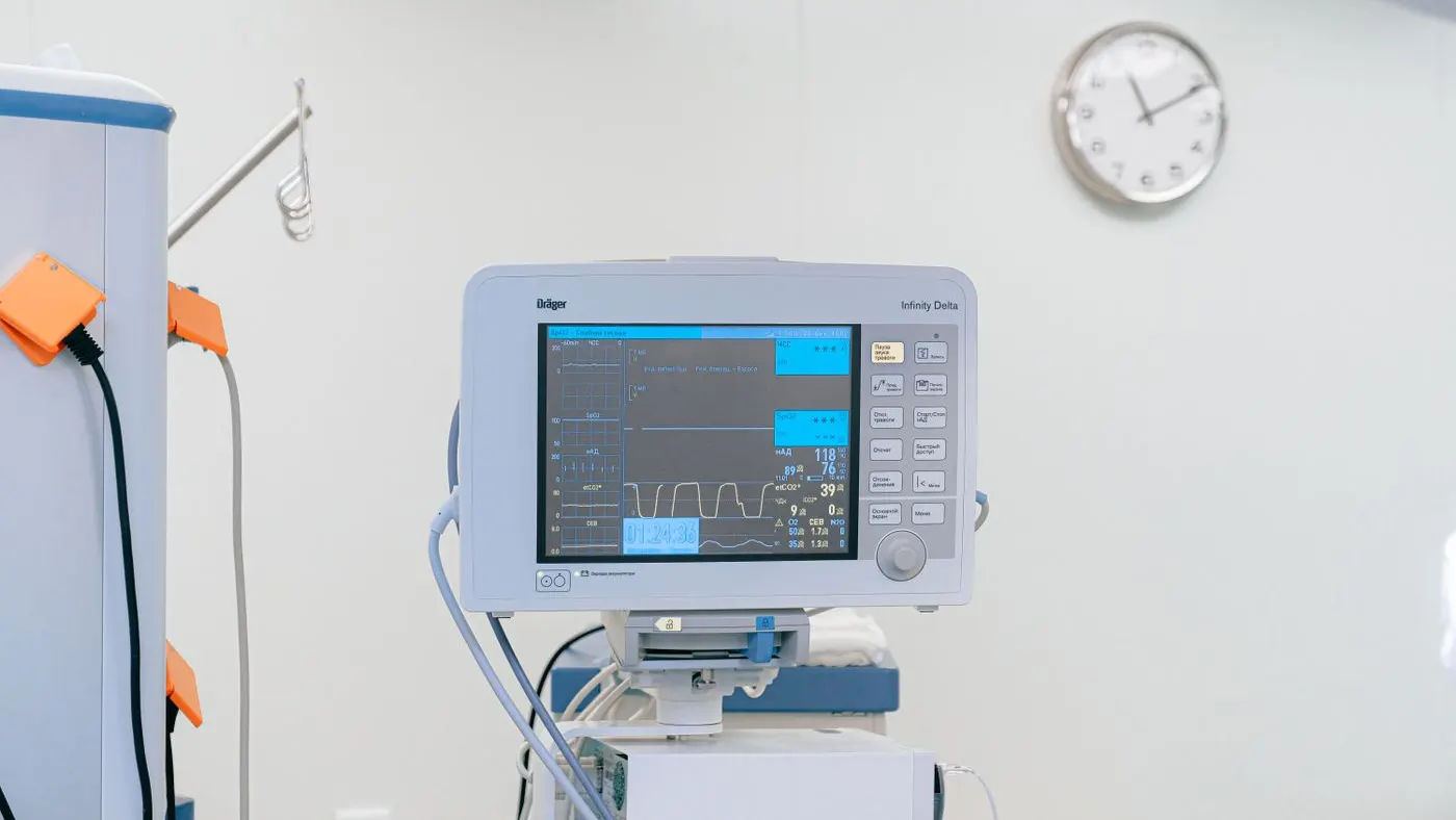 Monitor médico con pantalla azul que muestra los trazos del pulso, en una sala clara con un reloj redondo en la pared: imagen para la guía de la taquicardia